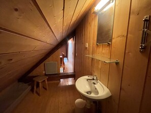 Ein Holzkamin mit schrägem Dach, einem weißen Waschbecken und einem Spiegel.