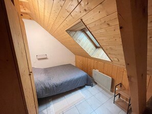 Ein kleiner Raum mit schrägem Dach, einem Bett, einer Heizung und einem Oberlicht.
