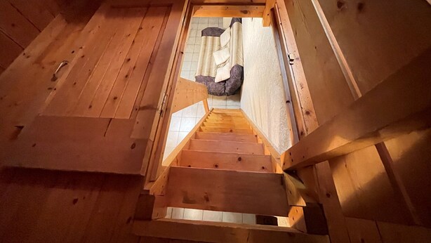 Una scala in legno conduce a un livello inferiore, con una parete in pietra e una finestra in alto.