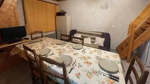 Una zona pranzo con tavolo apparecchiato per quattro persone, sedie in legno, televisore su un mobile e una scala in legno.