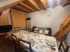 Ein Essbereich mit einem Tisch für vier Personen, Holzsesseln, einem Fernseher auf einem Schrank und einer Holztreppe.