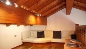 Ein gemütliches Schlafzimmer im Loft-Stil mit Holzbalkendecke, einer weißen Couch und einem Couchtisch aus Holz mit Büchern.