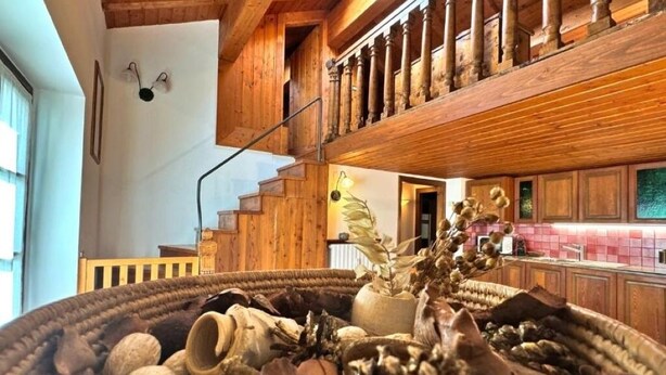 Ein rustikales Interieur mit einer Holztreppe, einer Essecke mit großem Holztisch und einer Küche mit Holzausstattung.
