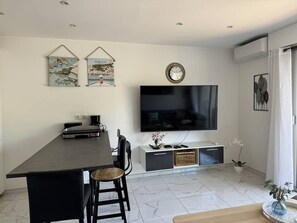 Un salon moderne doté d’un téléviseur à écran plat, d’une table à manger avec des chaises, d’une machine à café et d’œuvres d’art décoratives murales.