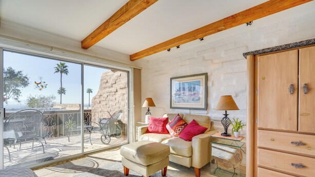 A spacious living area with a large window, a sofa, an ottoman, a wooden cabinet, and a small table with a lamp and plant. - Hike & Explore Dtwn Tucson! Relaxing Solo Escape (Tucson)