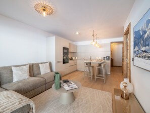 Ein modernes Wohnzimmer mit einer Couch, einem Couchtisch und einem Essbereich, im Hintergrund eine Küche.