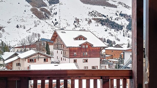 Un villaggio montano innevato con edifici in legno e una ringhiera di legno.