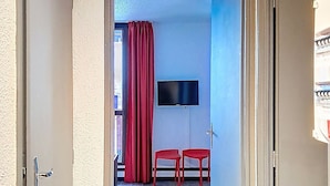 Una stanza con una televisione montata a parete, due sedie rosse e una tenda rossa.