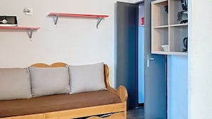 Una stanza con un divano in legno, due mensole a parete, una porta che dà su un'altra stanza e un angolo cottura con elettrodomestici.