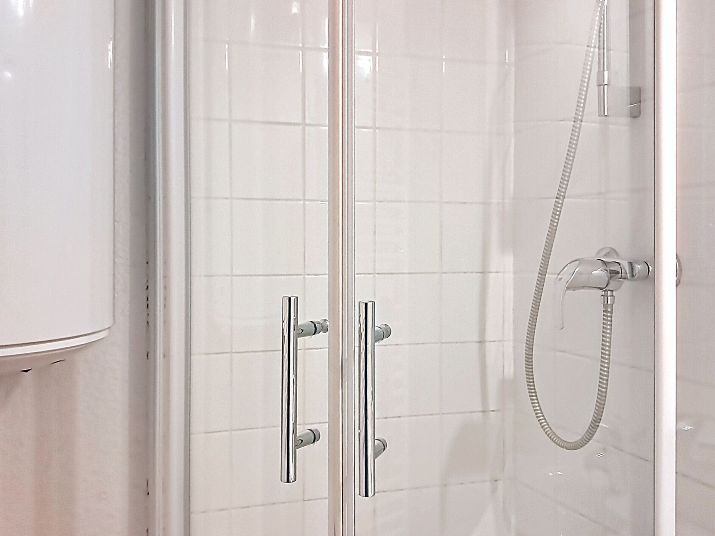 Eine Duschkabine mit Glas, chromfarbenen Armaturen und einer Handbrause.