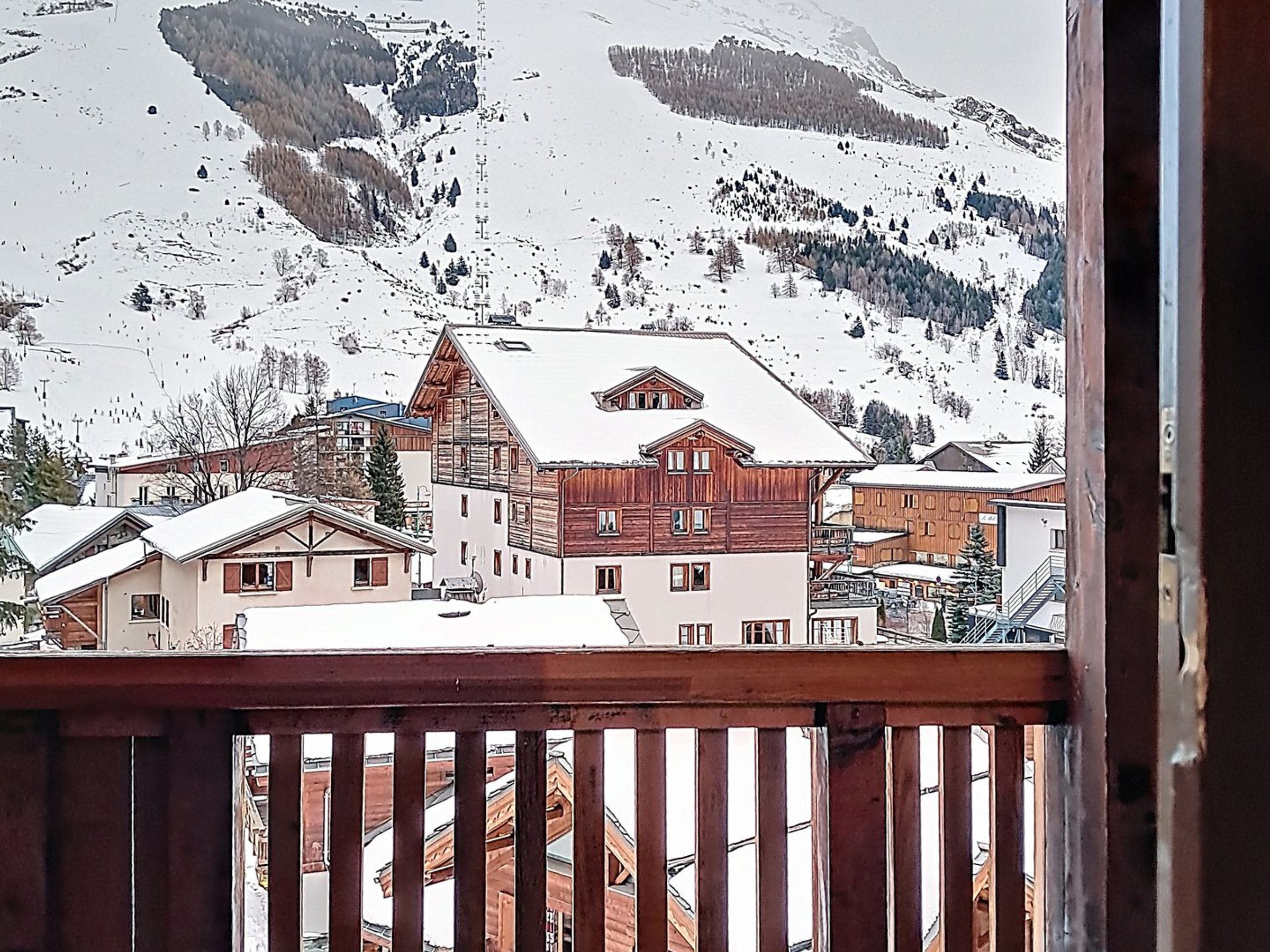 A snow-covered mountain village with wooden buildings and a wooden balcony railing.