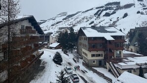 Un villaggio innevato con edifici in legno tradizionali, una seggiovia e una vista chiara sulle montagne circostanti.