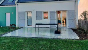 Ein modernes, zweistöckiges Haus mit gefliester Terrasse, einem Esstisch und einem kleinen Garten.