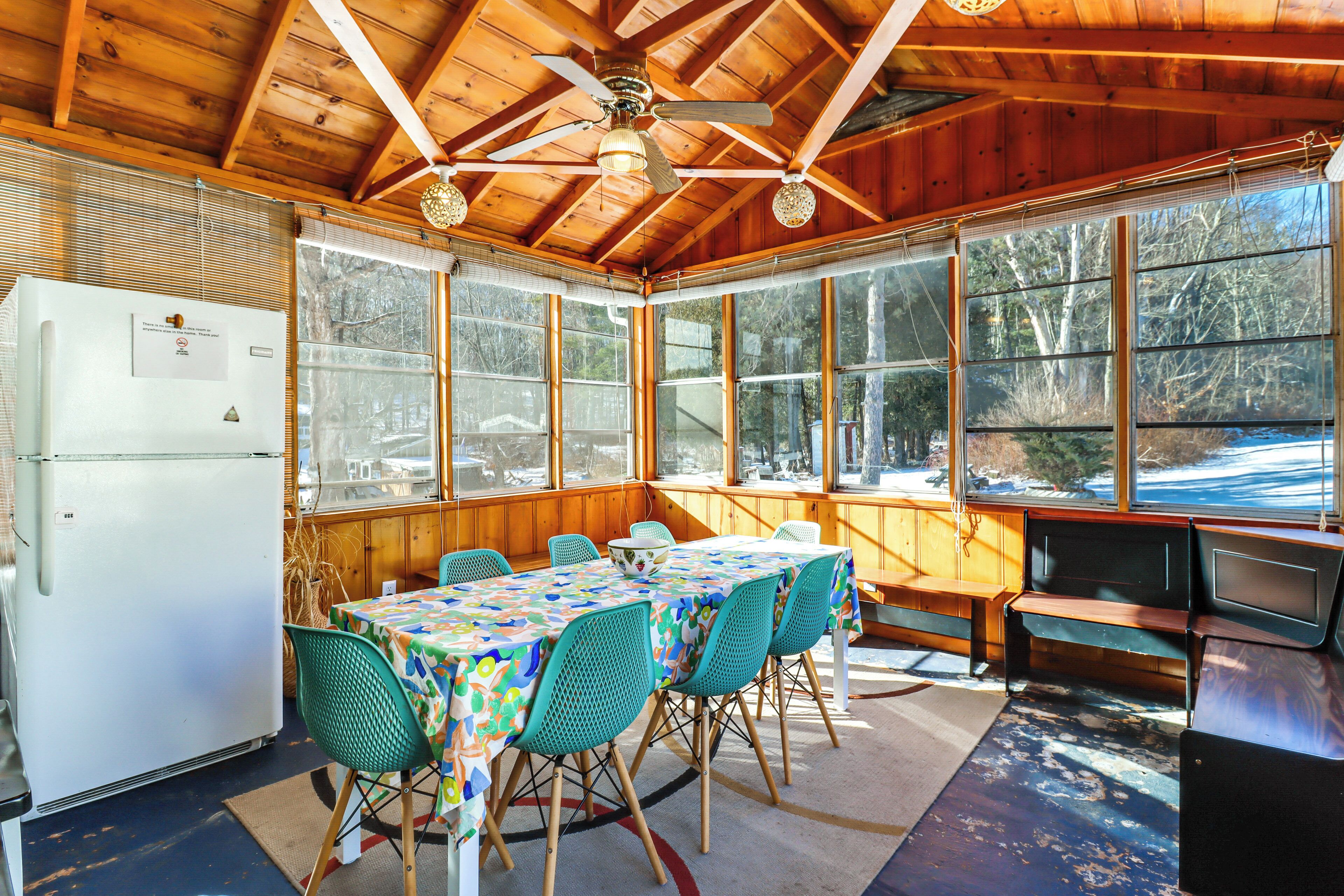 Une cabane en bois dotée d’un coin repas comprenant une table et des chaises, un réfrigérateur et de grandes fenêtres offrant une vue sur l’extérieur.