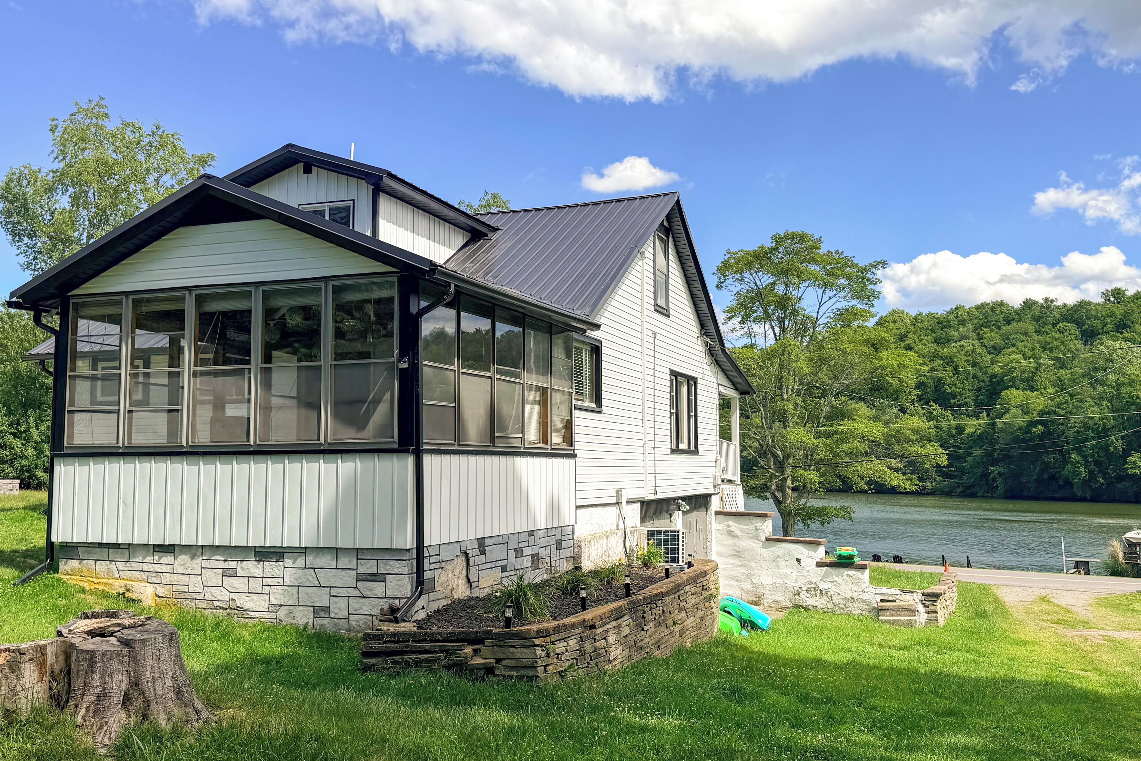 Une maison à deux étages avec de grandes fenêtres, des fondations en pierre et une vue sur un lac.