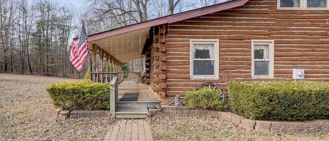 A log cabin with a porch, a flag, and a pathway leading to the entrance.