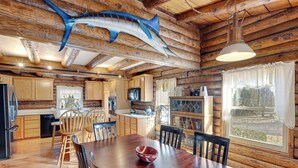 A wooden cabin interior with a dining table, chairs, a large fish mounted on the ceiling, and a window with curtains. - Hike, Fish & Boat Nearby! Bloomington Family Cabin (Bloomington)