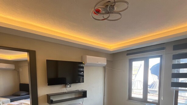 A hotel room with two beds, a small desk, a TV, and a window with blinds. - rema house (Gemlik)