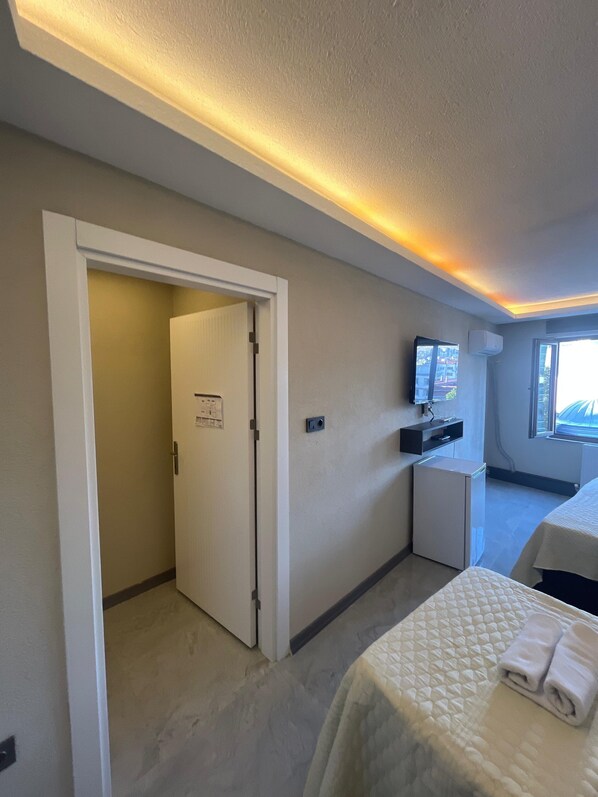 A hotel room with a bed, a desk, a small refrigerator, an air conditioning unit, and a door leading to another room. - rema house (Gemlik)