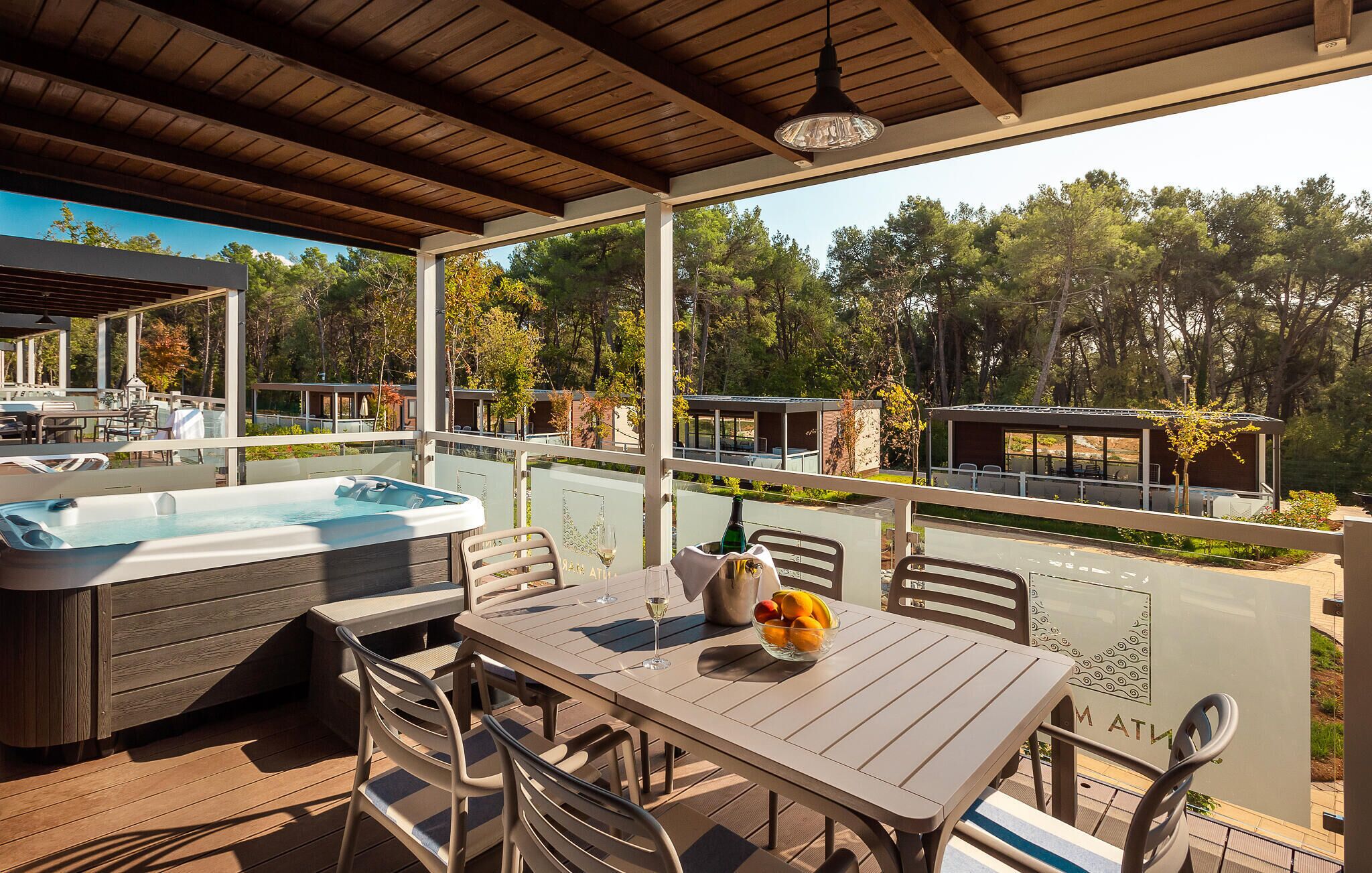 Un espace extérieur abrité comprenant un jacuzzi, une table avec des chaises et une vue sur les arbres et les bâtiments environnants.