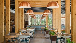 Un restaurant avec des poutres en bois, des suspensions en cuivre et un mur de pierre en arrière-plan. Les tables sont disposées avec des chaises et des plantes en pot.