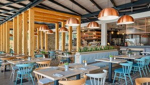 Un restaurant avec des poutres en bois, des chaises bleues et des suspensions en cuivre.