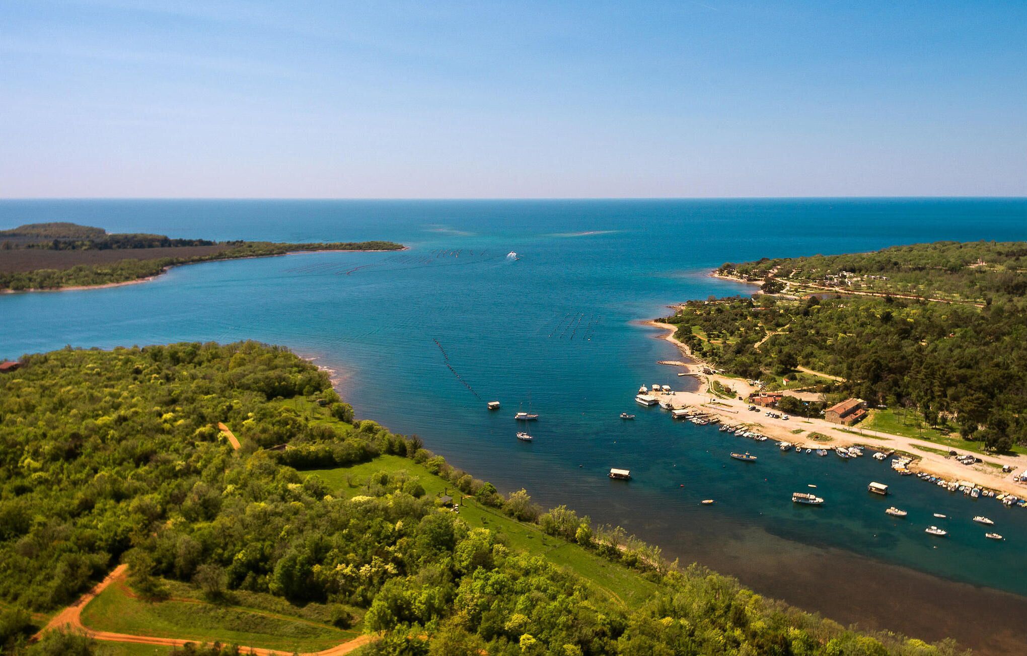 Una zona costera con vista despejada al mar, barcos y una pequeña playa con edificios.