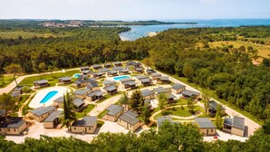 A resort with multiple bungalow-style accommodations, a central swimming pool, and a view of a lake and distant shoreline. - Lovely (sta)caravan in Vabriga (Vabriga)