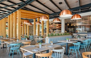 Ein Restaurant mit Holzbalken, blauen Stühlen und Kupfer-Pendelleuchten.