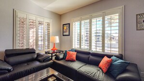 A living room with a black leather sofa, a glass coffee table, and a framed picture on the wall. - Pool & Personal Bar! 4 Mi to Downtown Mesa Home (Mesa)