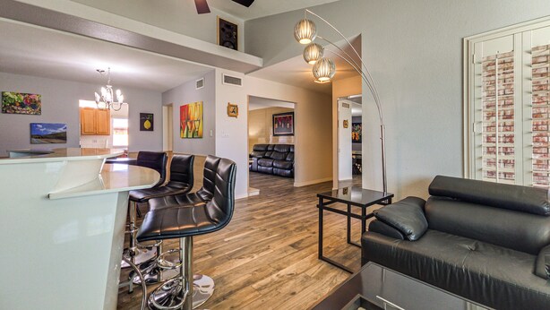 A modern living room with a black leather sofa, a dining area with a bar stool, and a ceiling fan. - Pool & Personal Bar! 4 Mi to Downtown Mesa Home (Mesa)