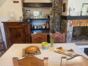 A cozy dining area with a wooden table, chairs, and a fireplace. There are various dishes and a glass of wine on the table. - "L'Ecrin du Mercantour" in the heart of Vésubie, at the gateway to the Mercantour. (belvédère)