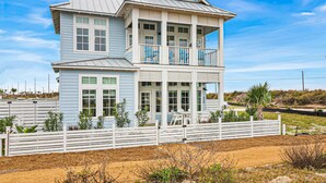 A two-story beach house with a balcony, a fenced yard, and a sandy beach in the background. - Palmilla Resort home with heated pool, golf, beach access, balconies, W/D, AC (Port Aransas)