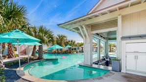 A pool area with a circular pool, palm trees, and a covered seating area with umbrellas. - Palmilla Resort home with heated pool, golf, beach access, balconies, W/D, AC (Port Aransas)