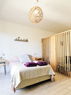 Quarto com cama, mesa de cabeceira, prateleira na parede e divisória de madeira.
