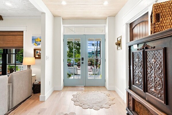 Un pasillo con una puerta azul claro, suelo de madera, alfombra redonda y un mueble de madera oscura con tallas detalladas.