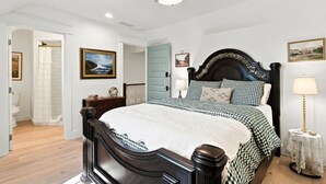A bedroom with a large bed, a bedside table, a lamp, and a door leading to a bathroom.