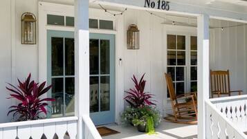 A white building with a porch, a rocking chair, and potted plants.