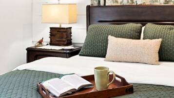 A neatly made bed with a green quilt, a wooden tray with a book and mug, a nightstand with a lamp, and a patterned wall.