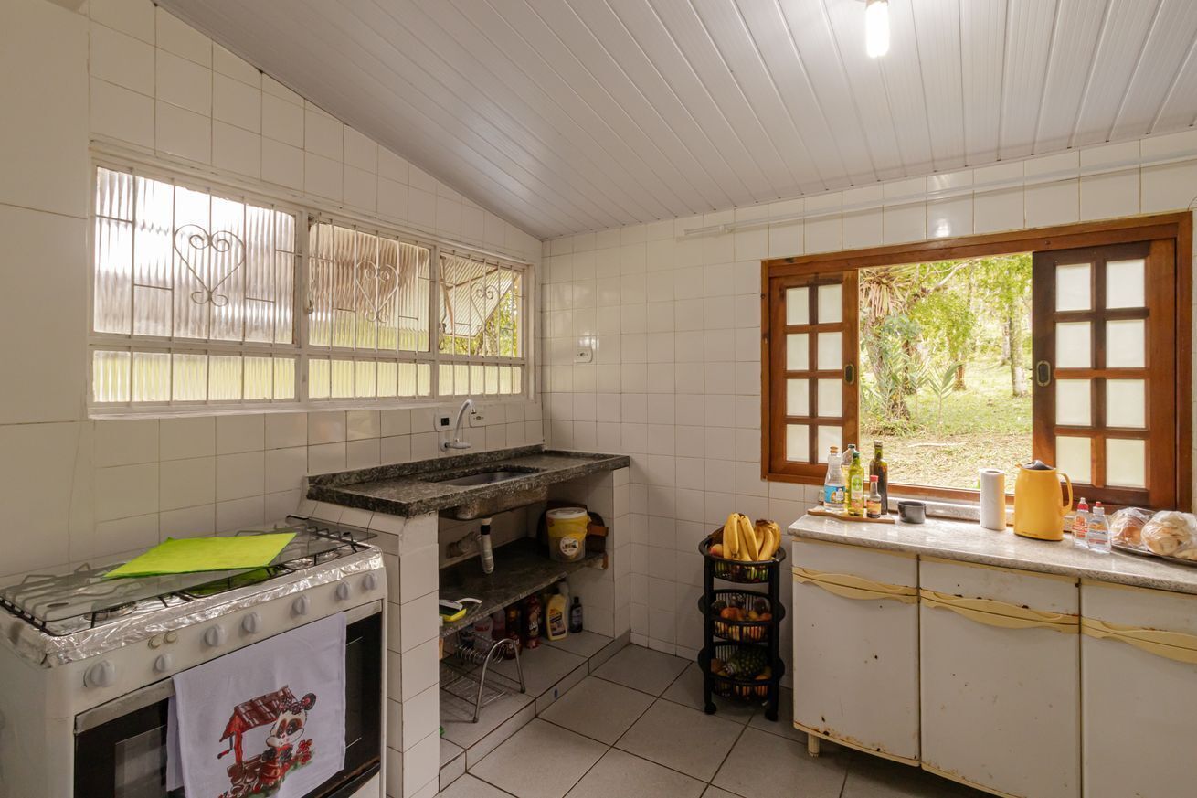 Uma cozinha com fogão a gás, pia, janela com vista para vegetação e bancada com diversos objetos.