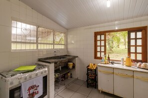 Eine Küche mit Gasherd, Spüle, einem Fenster mit Blick auf Grünflächen und einer Arbeitsplatte mit diversen Gegenständen.