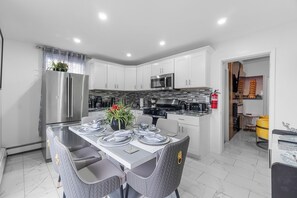 Una cocina moderna con armarios blancos, electrodomésticos de acero inoxidable y un comedor con una mesa dispuesta para cuatro.