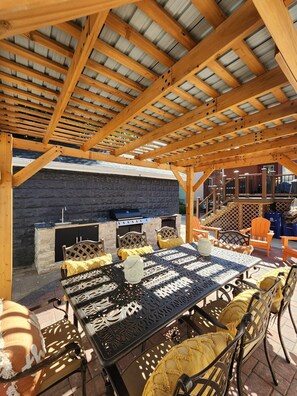 Un patio al aire libre con una parrilla, asientos y una zona cubierta con vigas de madera.