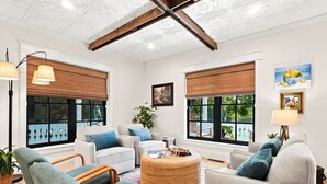 A spacious living area with a high ceiling, large windows with blinds, and a central round coffee table.