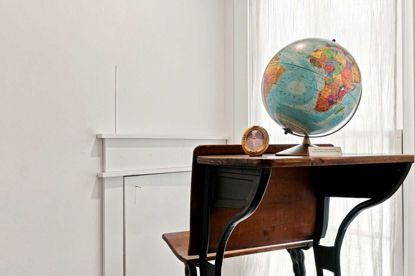 Un bureau avec un globe terrestre et un tableau encadré, le tout placé devant un mur blanc.