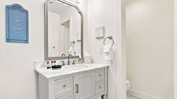 A bathroom with a white vanity, a large mirror, a towel rack, and a sign with text.