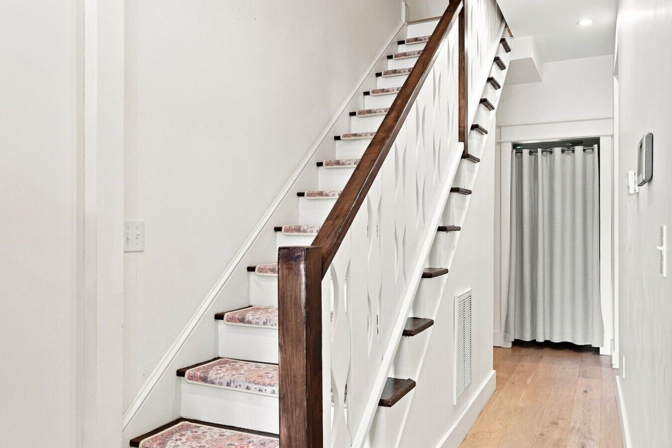 Una escalera con barandillas de madera y paredes blancas, que conduce a una habitación con una puerta y un ventanal.