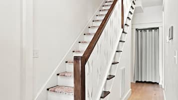 Una escalera con barandillas de madera y paredes blancas, que conduce a una habitación con una puerta y un ventanal.