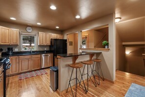 A modern kitchen with wooden cabinets, a black refrigerator, a sink, and a bar area with stools. - Big Sky Escape - Private Patio & Grill (Big Sky)