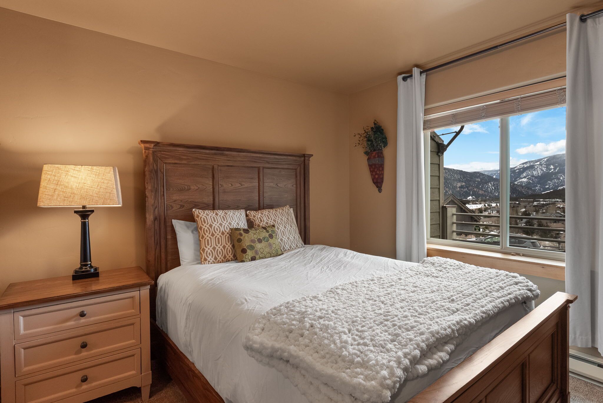 Une chambre à coucher avec un lit en bois, une table de chevet, une lampe et une fenêtre donnant sur les montagnes.